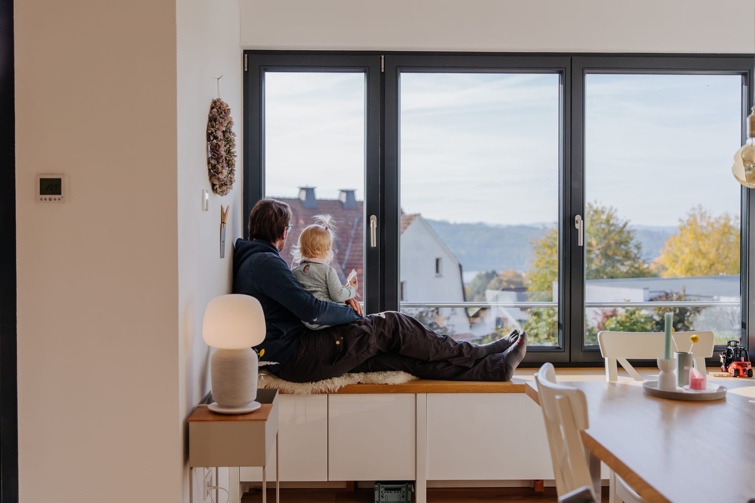 A father and child sitting in a window nook looking out through open tilt-turn windows