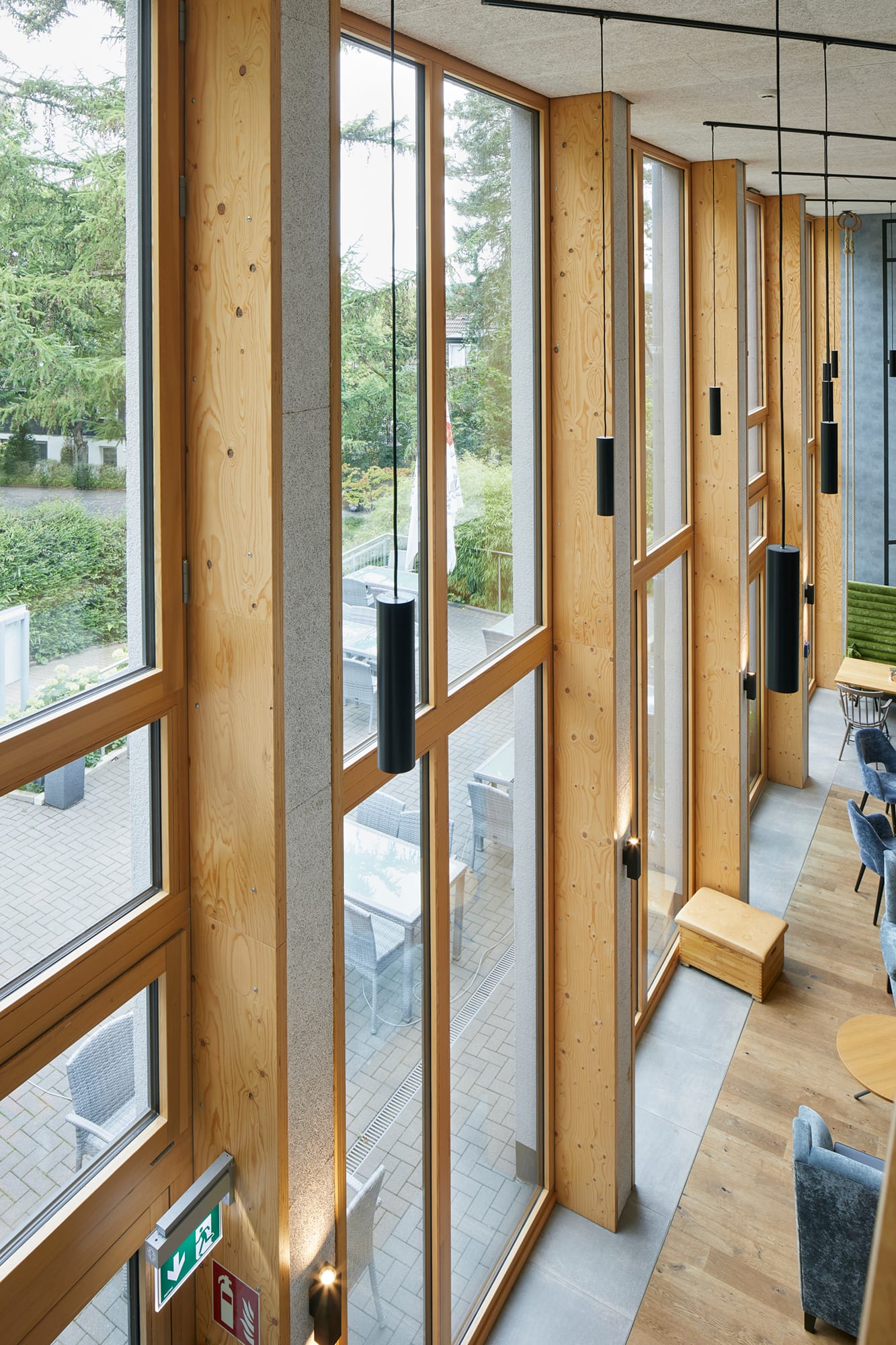 Floor-to-ceiling wood-framed windows in a modern building interior with hanging pendant lights